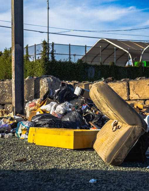Three large black rubbish bags made of plastic or similar material, filled and somewhat lumpy in appearance, are positioned along the edge of a paved sidewalk, adjacent to a low curb. The bags are pla